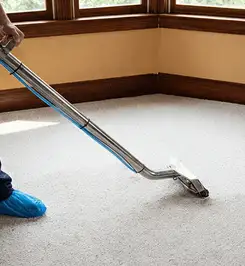 Steam carpet cleaning technician using a hot-water extraction wand on a residential carpet, wearing blue protective shoe covers Staten Island, NY.