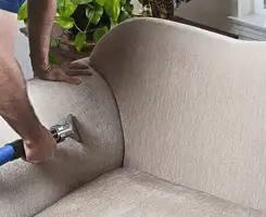 Professional upholstery cleaner deep-cleaning a fabric sofa with a handheld extraction tool and hose in Staten Island, NY.